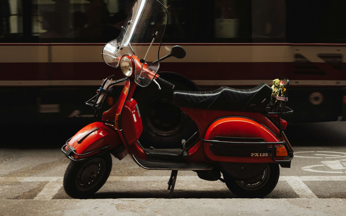 Scooter 125 cm³ rouge stationné en ville devant un tramway